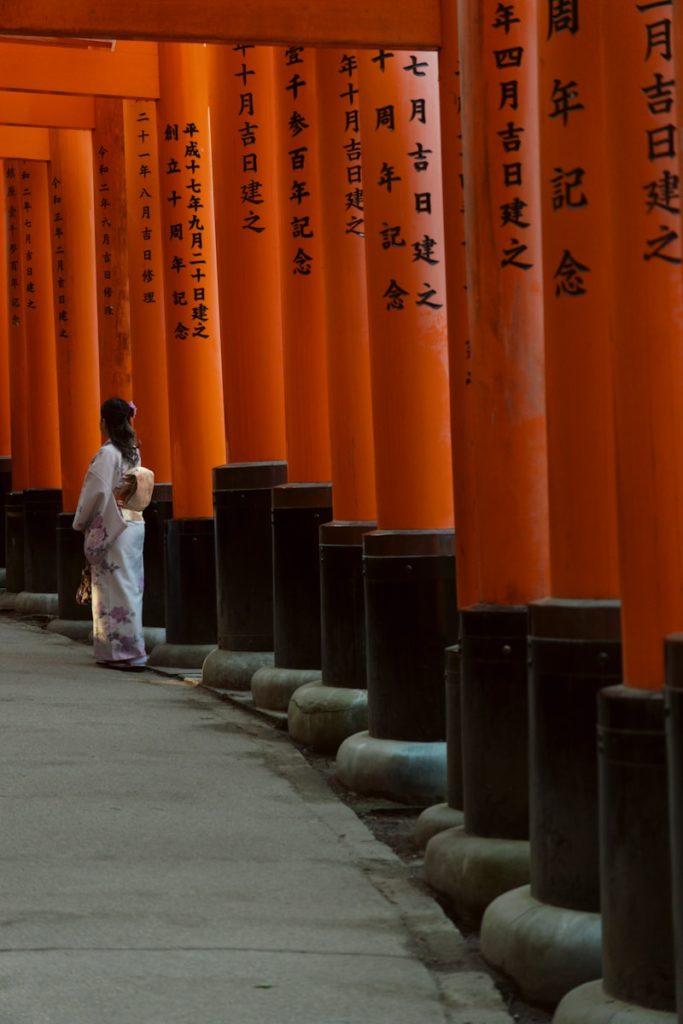 a woman in a white kimono is standing in front of a row of orange