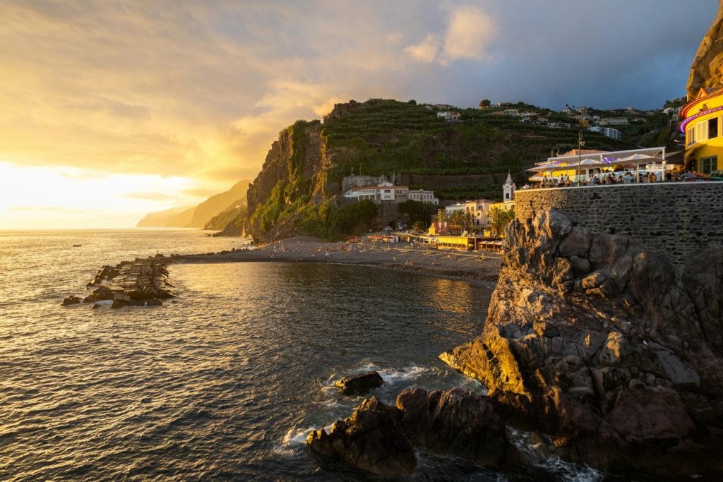 The sun is setting over the ocean with houses on the cliff