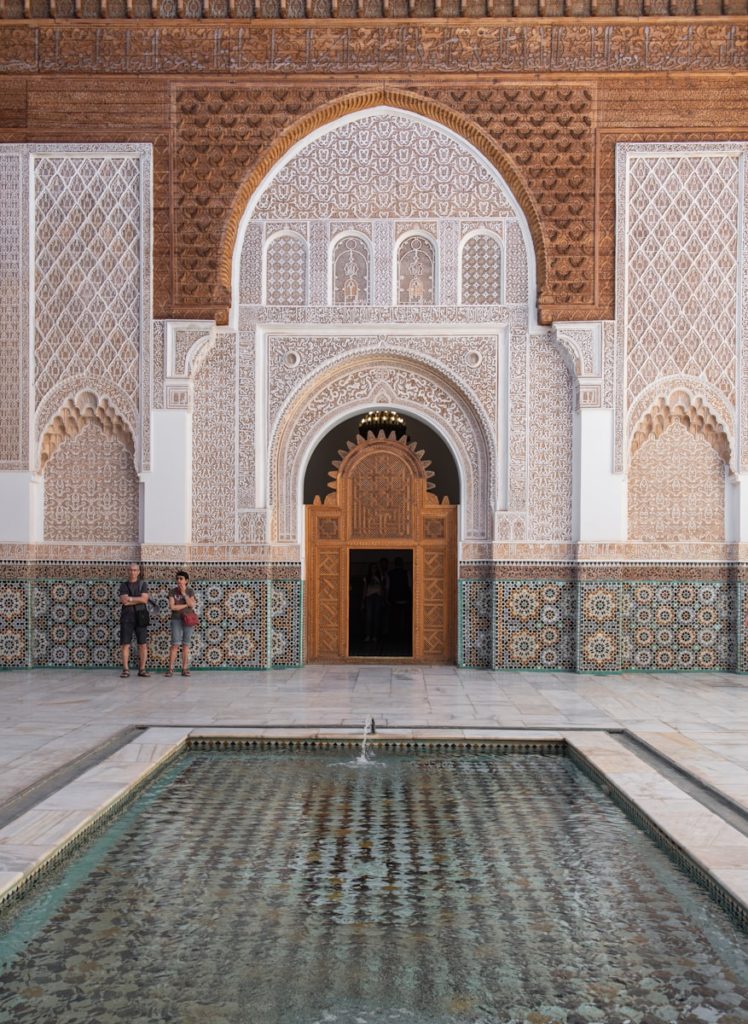 Two people standing in front of a building with a fountain