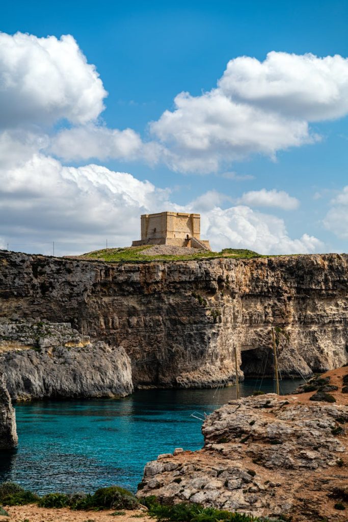 Explore the stunning azure waters and rugged cliffs of Malta, featuring a historic fort under a bright blue sky.