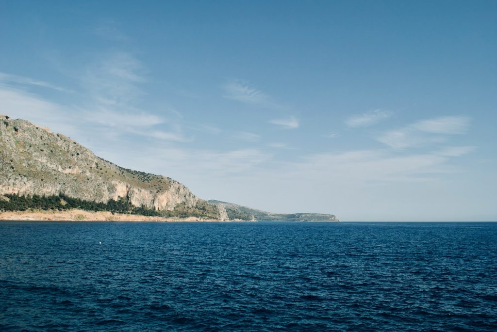 green and brown mountain beside blue sea under blue sky during daytime